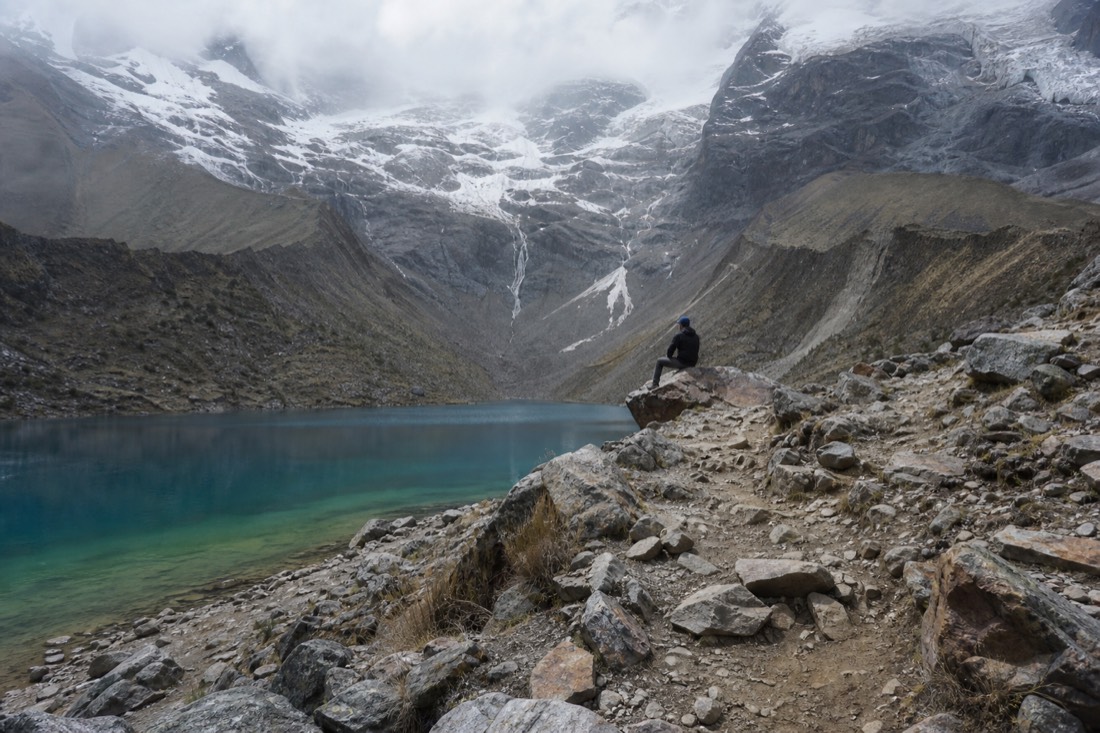 Hiker sitting alone on rocks at the far end of the Humantay shore path away from the main viewpoint