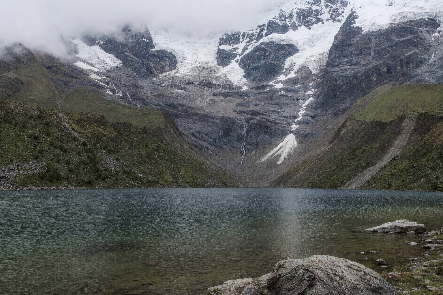 Humantay Lake under low grey cloud in the wet season, its surface slate-coloured beneath the glacier
