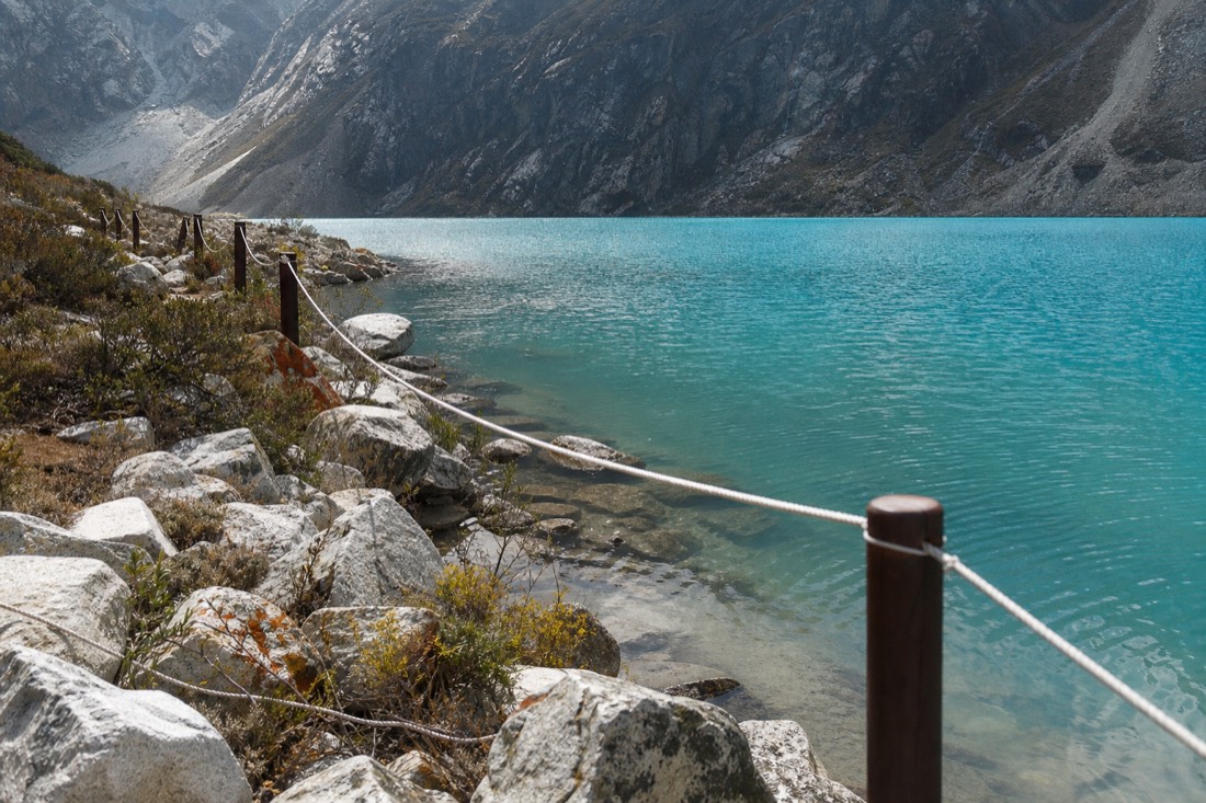 Simple rope barrier line strung along the rocky edge of a turquoise glacial lake marking the protected waterline, no people