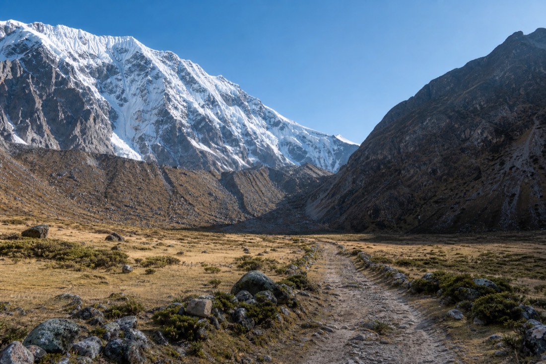 The wide Soraypampa plain at first light with the unpaved trailhead track and Salkantay's snow slopes rising behind, empty trail
