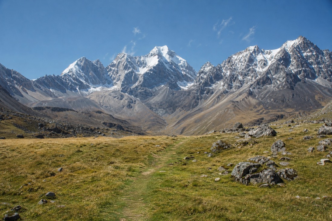 Gentle grassy walking path across the high Soraypampa plain with snow-dusted Andean peaks in the distance and no people