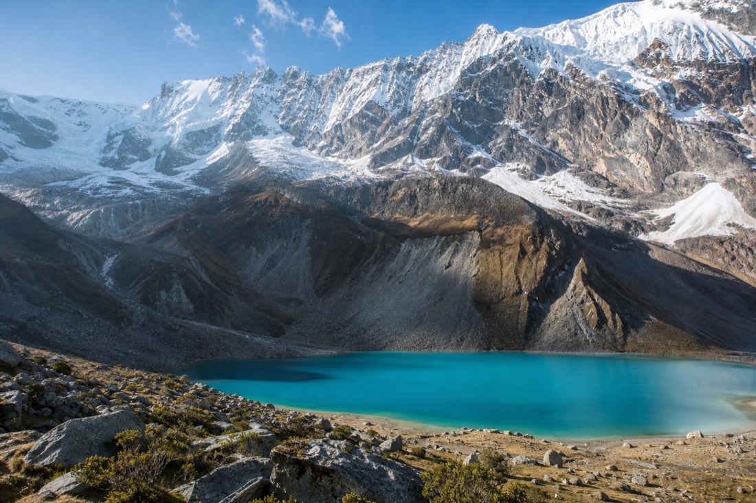 Turquoise glacier lake in a rock bowl below an icy peak with the Salkantay massif rising behind in clear early light