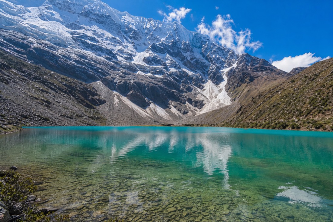 Humantay Lake glowing deep turquoise under clear early morning light with the glacier wall reflected, no people on the shore