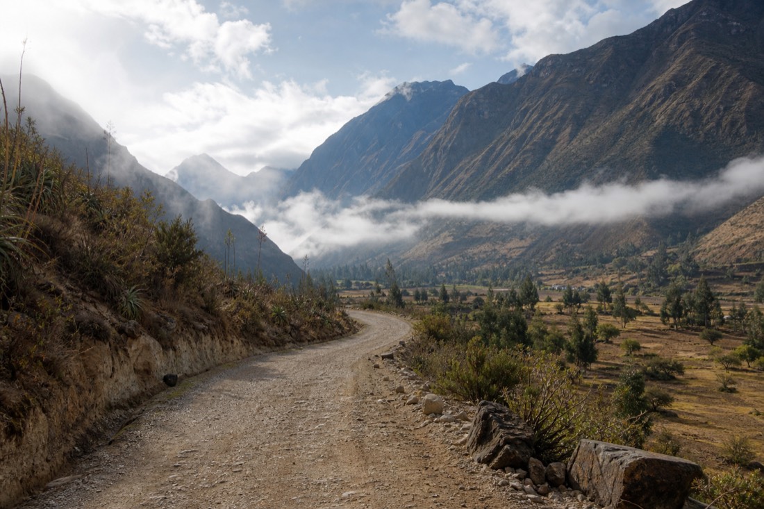 Unpaved mountain road winding through the Limatambo valley toward Mollepata under morning cloud, empty road