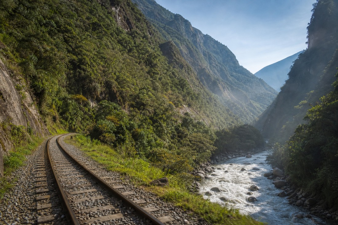 The Urubamba river gorge with a railway line running beside green cloud-forest slopes toward Aguas Calientes, no people